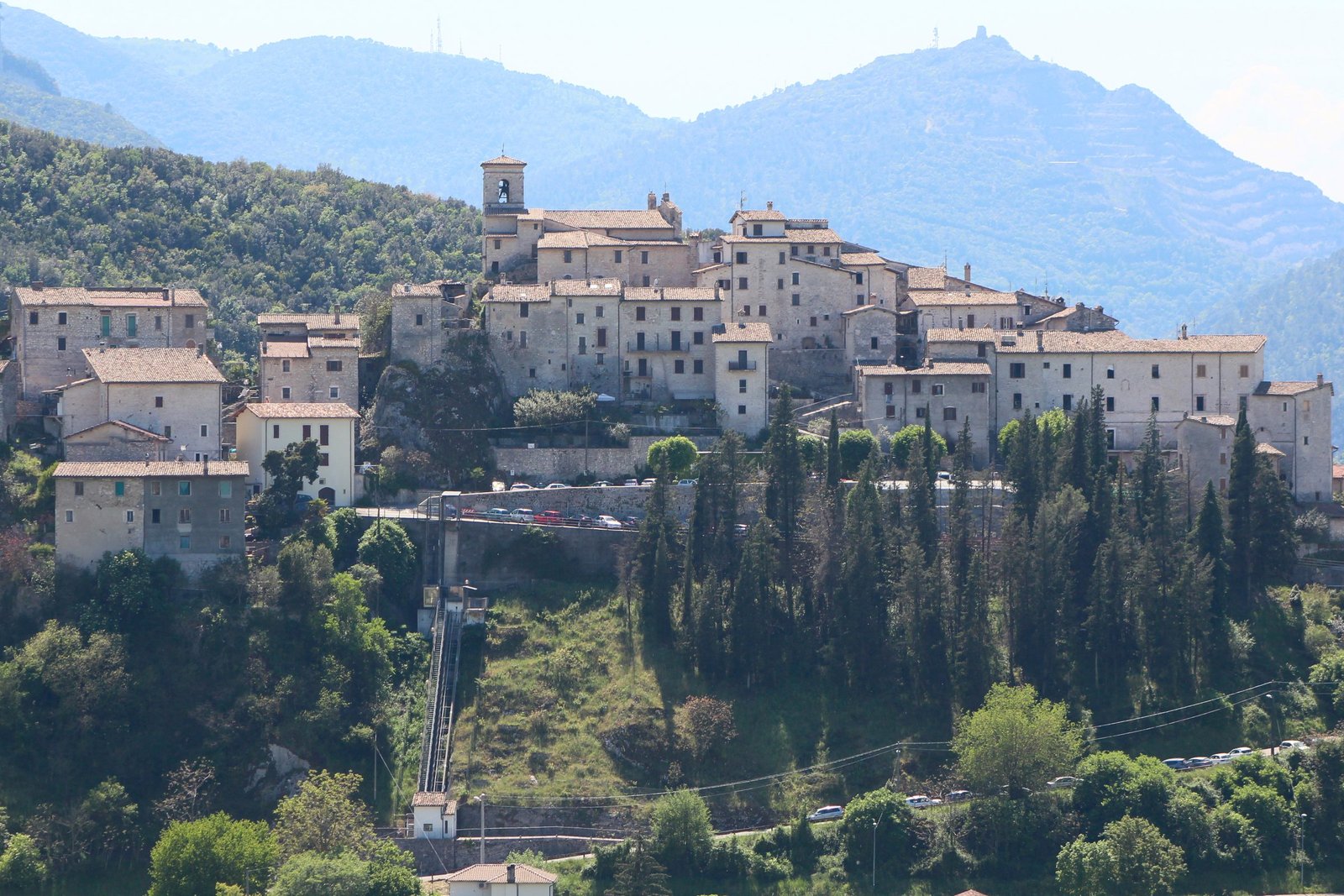 The stone village of Casteldilago packed onto its rock spur above the Nera valley, with cypresses in the foreground