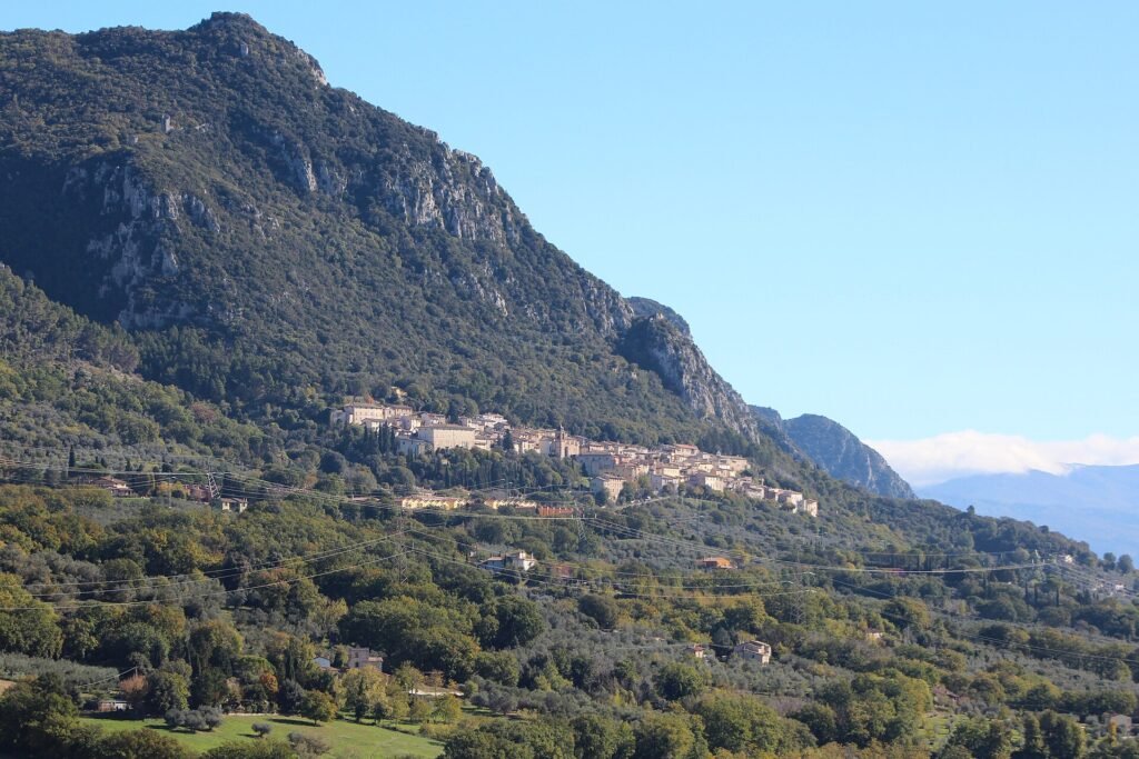 Il borgo di Cesi disteso ai piedi di una montagna ripida e rocciosa, con uliveti e boschi sotto