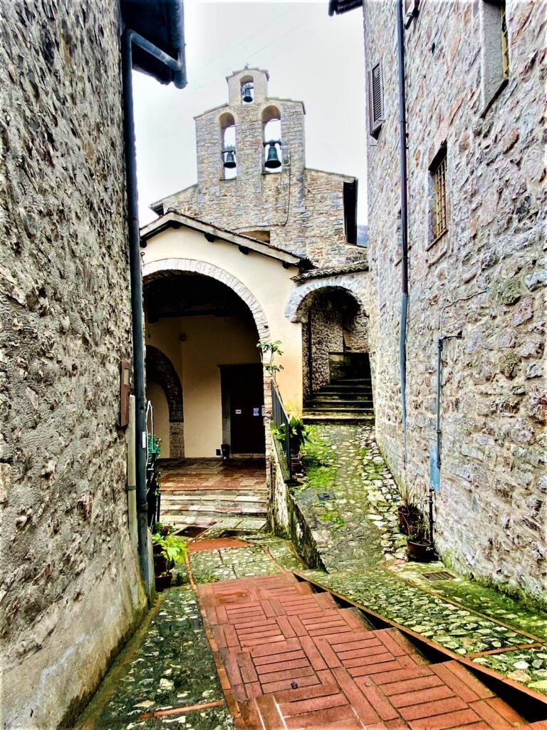 Vicolo in pietra con un percorso in mattoni rossi che sale al portico ad arco di una chiesa con campanile a vela