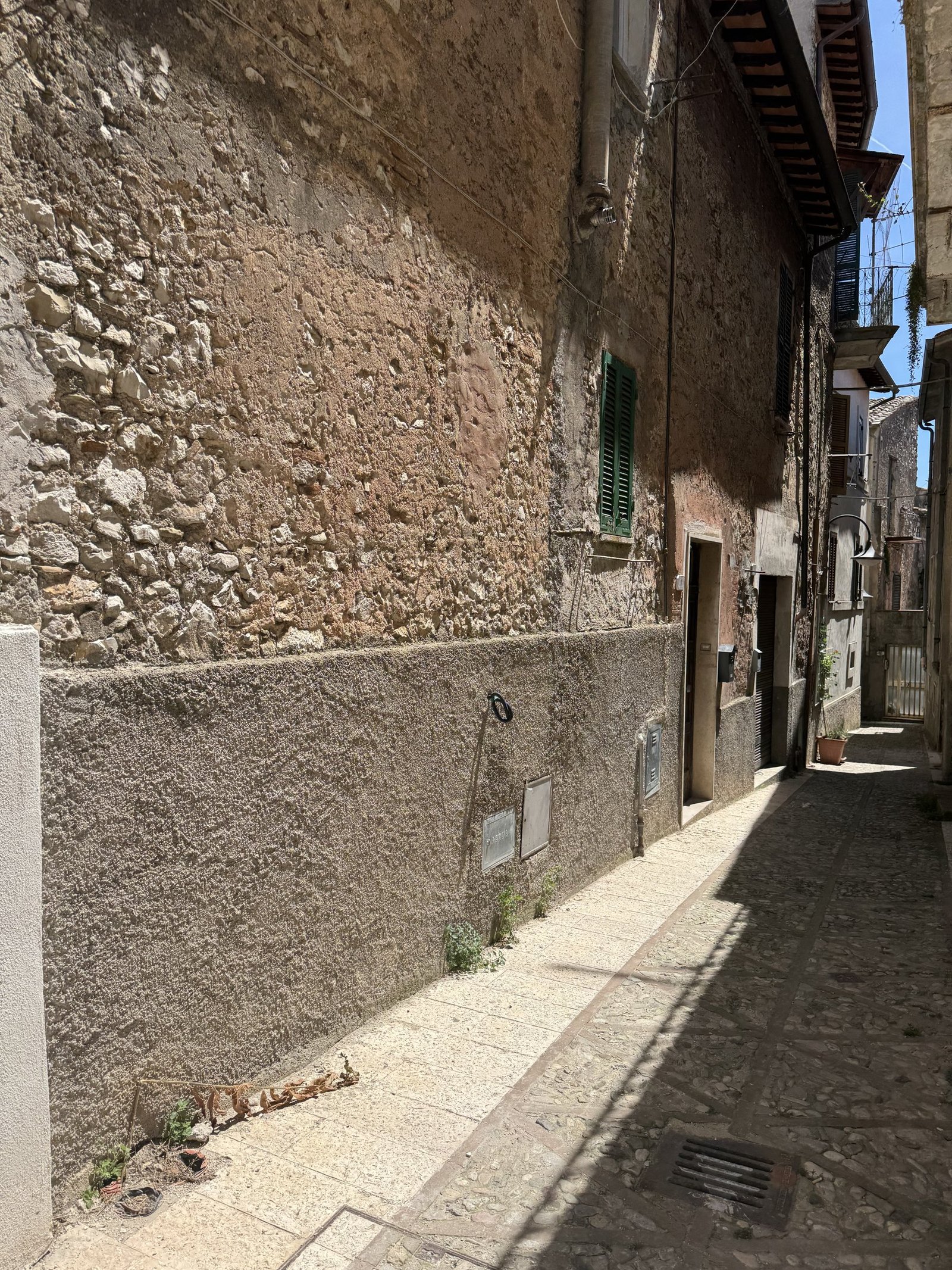 A narrow lane in Collestatte between a rough stone wall and shuttered houses