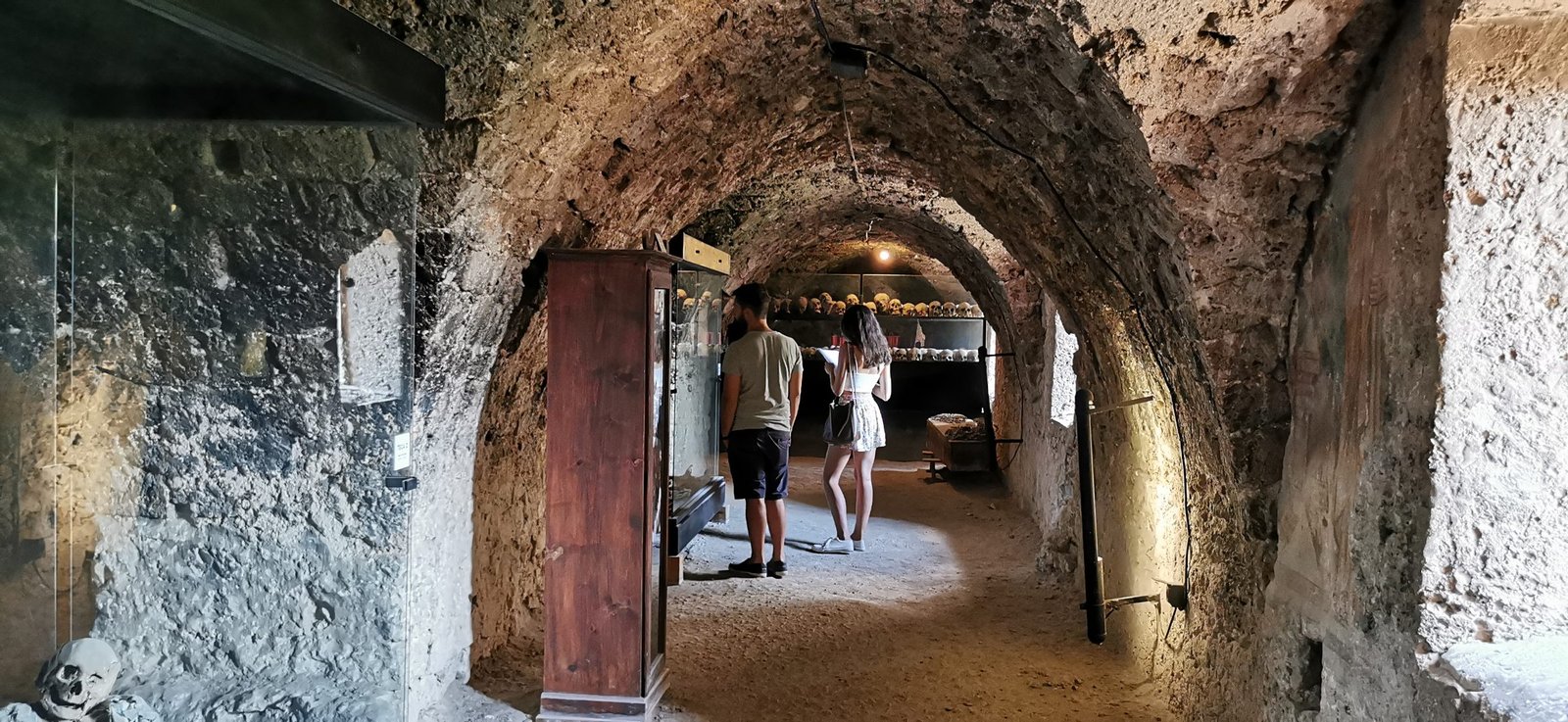 The vaulted stone crypt beneath the church at Ferentillo, where the mummies are displayed, with two visitors walking through