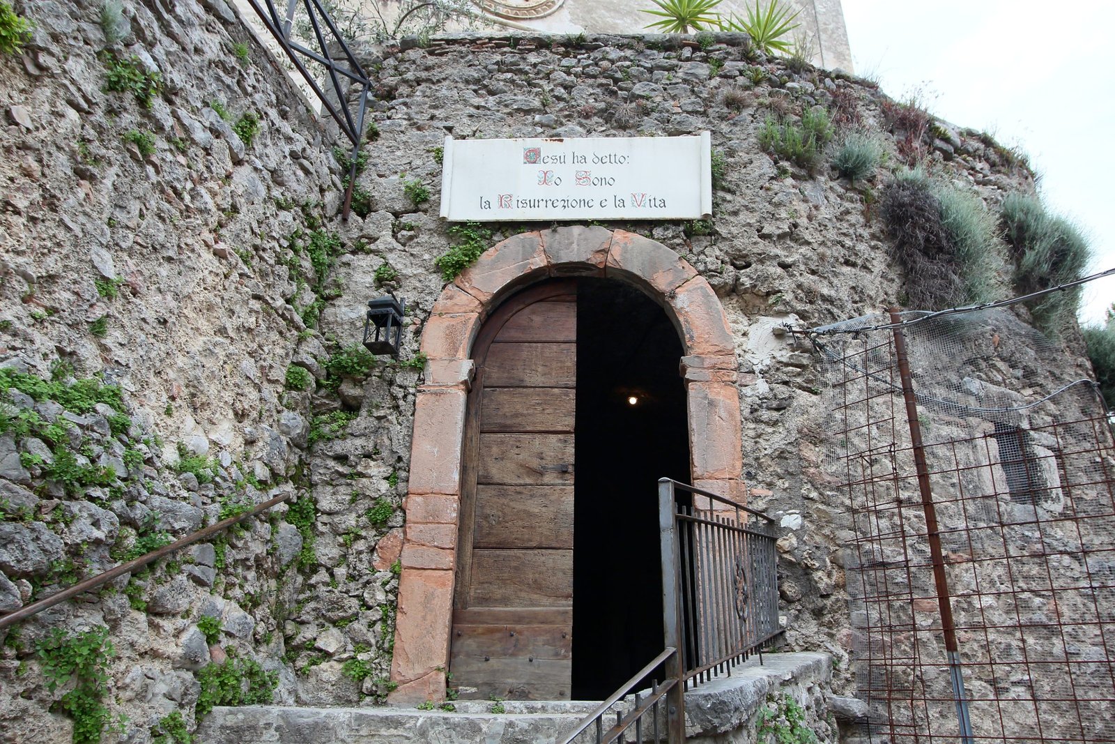An arched stone doorway with a marble plaque above it, the entrance to the mummy museum at Precetto di Ferentillo