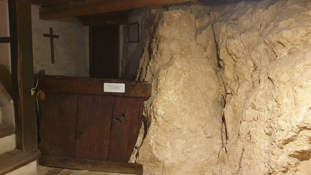 Un semplice pulpito di legno addossato alla roccia viva dentro il santuario, con una croce di legno alla parete