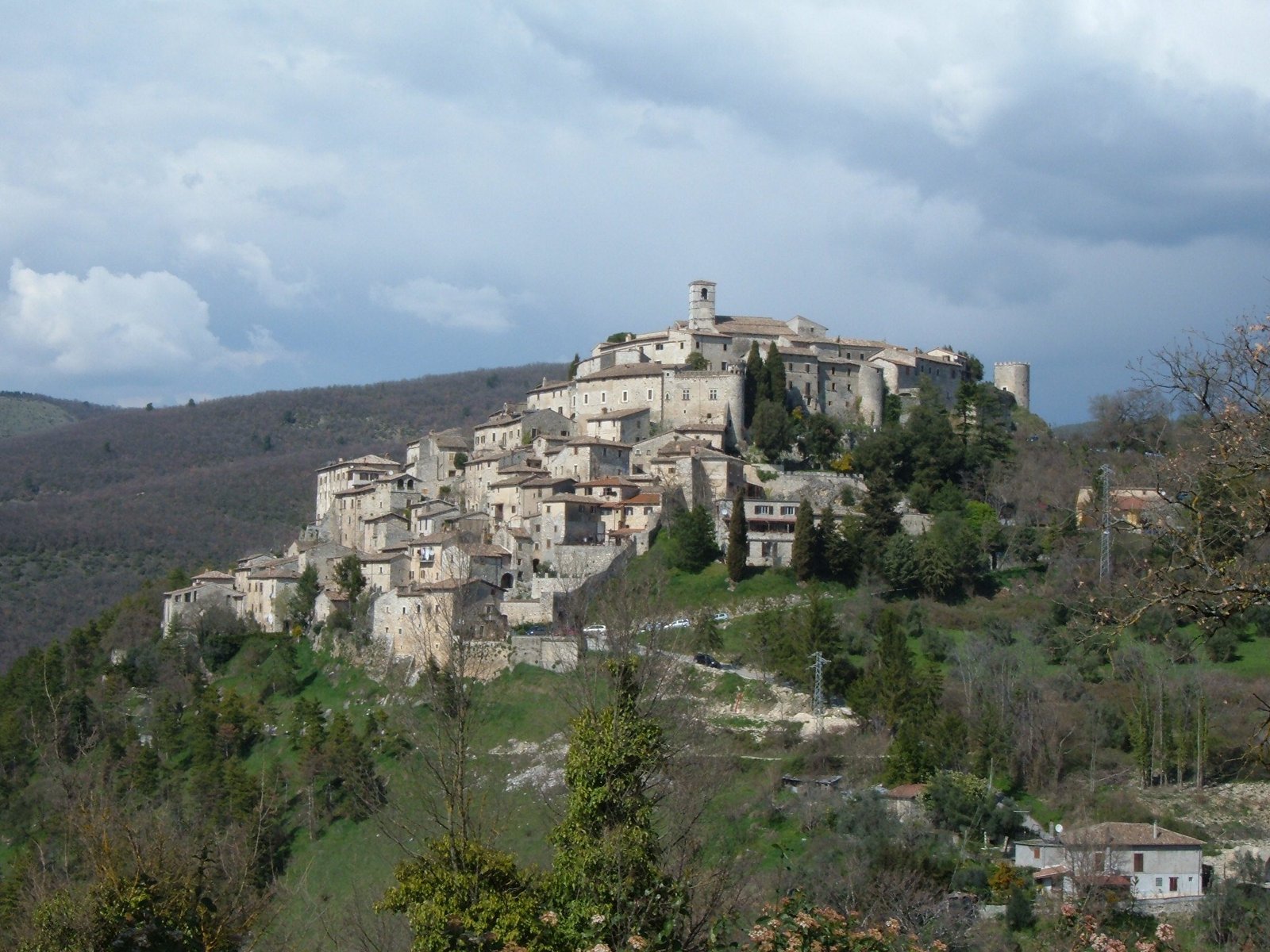 The hilltop village of Labro seen across wooded slopes under a cloudy sky