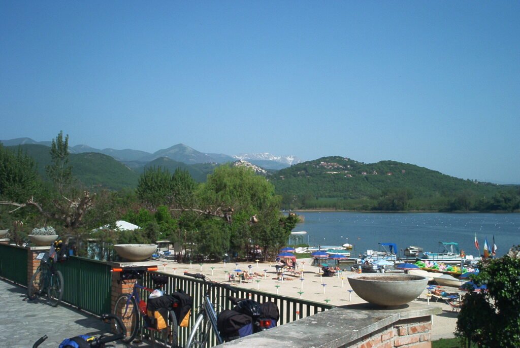 Terrazza con ringhiera e biciclette sopra una piccola spiaggia sul lago di Piediluco, colline e montagne sullo sfondo