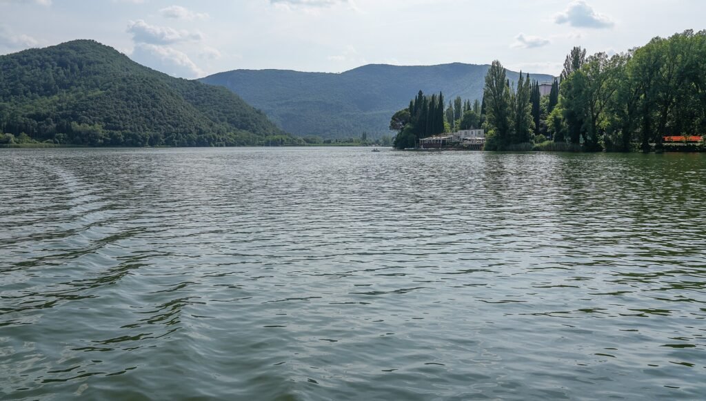 Ampia vista sulla superficie increspata del Lago di Piediluco verso colline boscose e montagne, cielo parzialmente nuvoloso