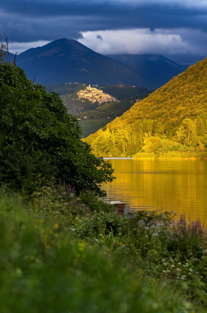 Il Lago di Piediluco dorato nella luce della sera, Labro illuminato sulla sua collina, montagne scure e nuvole dietro