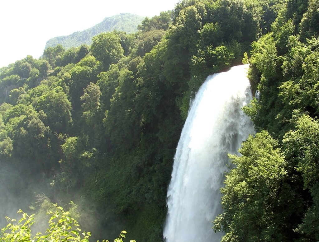 A white column of water plunging down a cliff between steep, densely wooded slopes