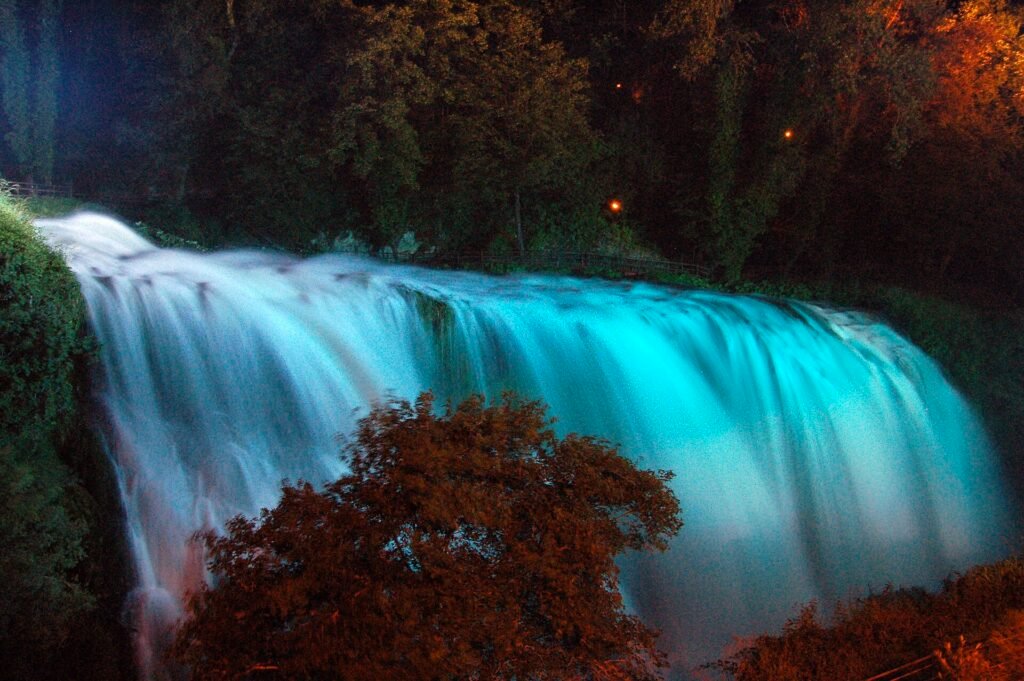 La Cascata delle Marmore di notte, l’ampio getto illuminato di turchese tra alberi scuri