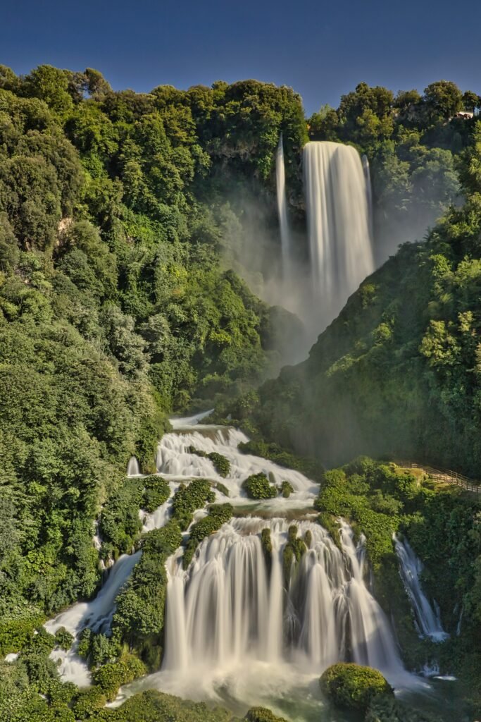 Tutta l'altezza della cascata vista dal basso: il lungo salto superiore e ampie cascate bianche tra rocce e boschi
