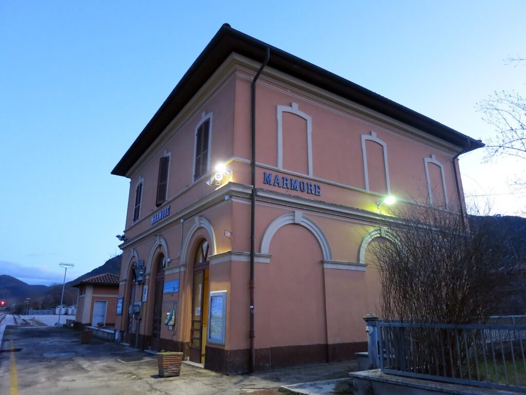 La stazione di Marmore, un edificio rosa a due piani al tramonto, con il nome in lettere blu sulla facciata