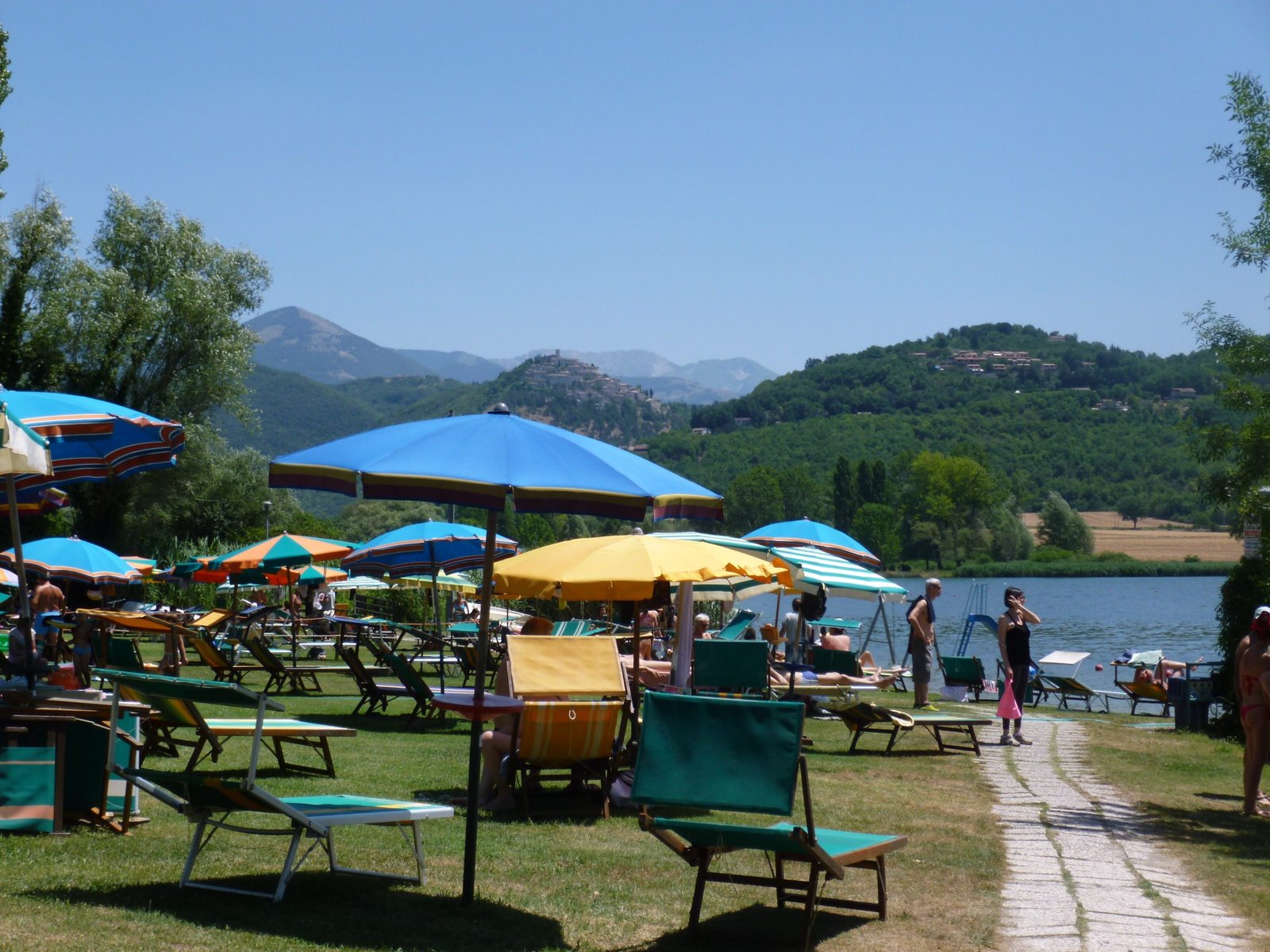 Sun loungers and parasols on the grass at the edge of Lake Piediluco, with wooded hills beyond