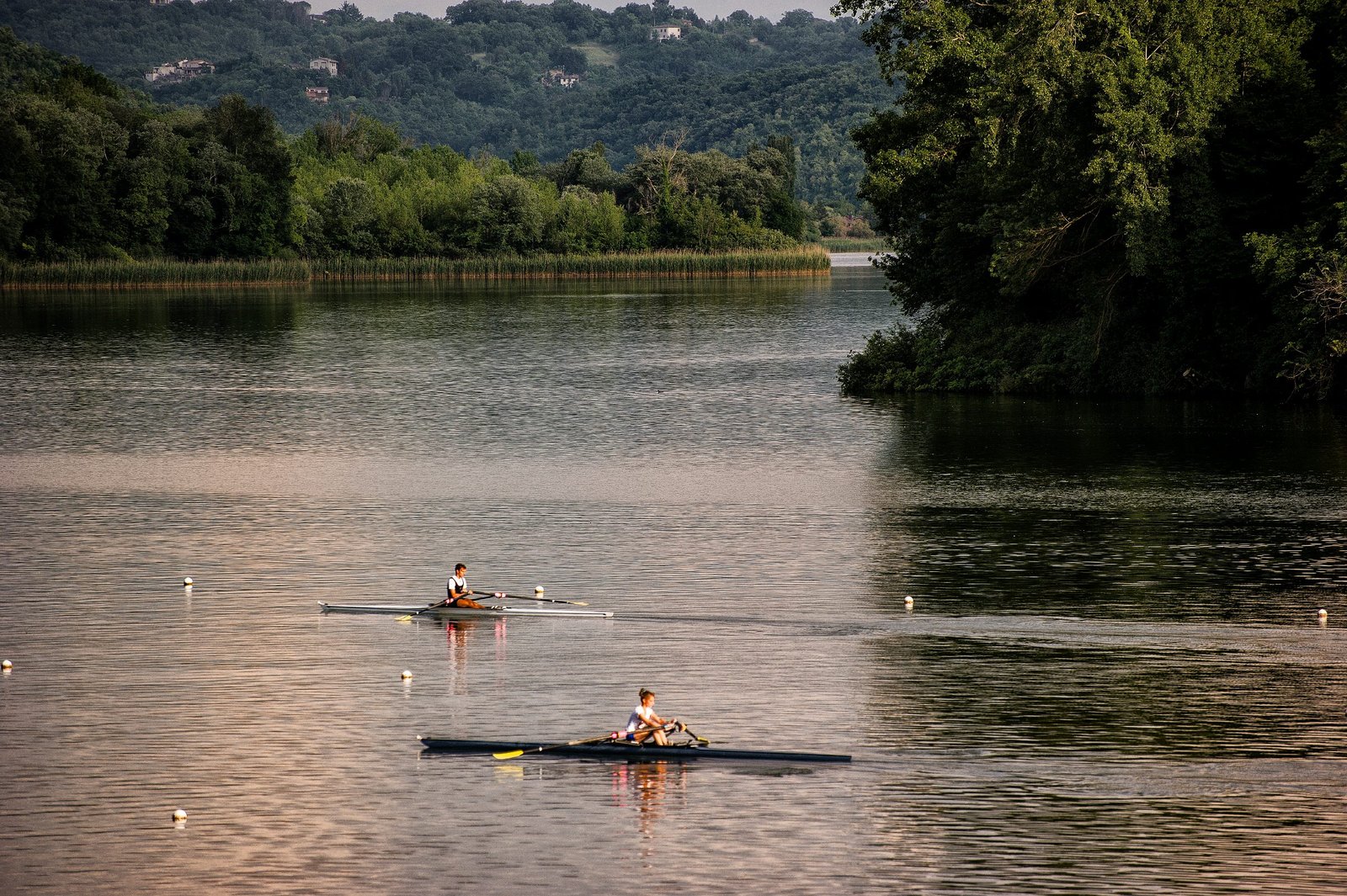Two rowing boats out on Lake Piediluco with wooded shores behind