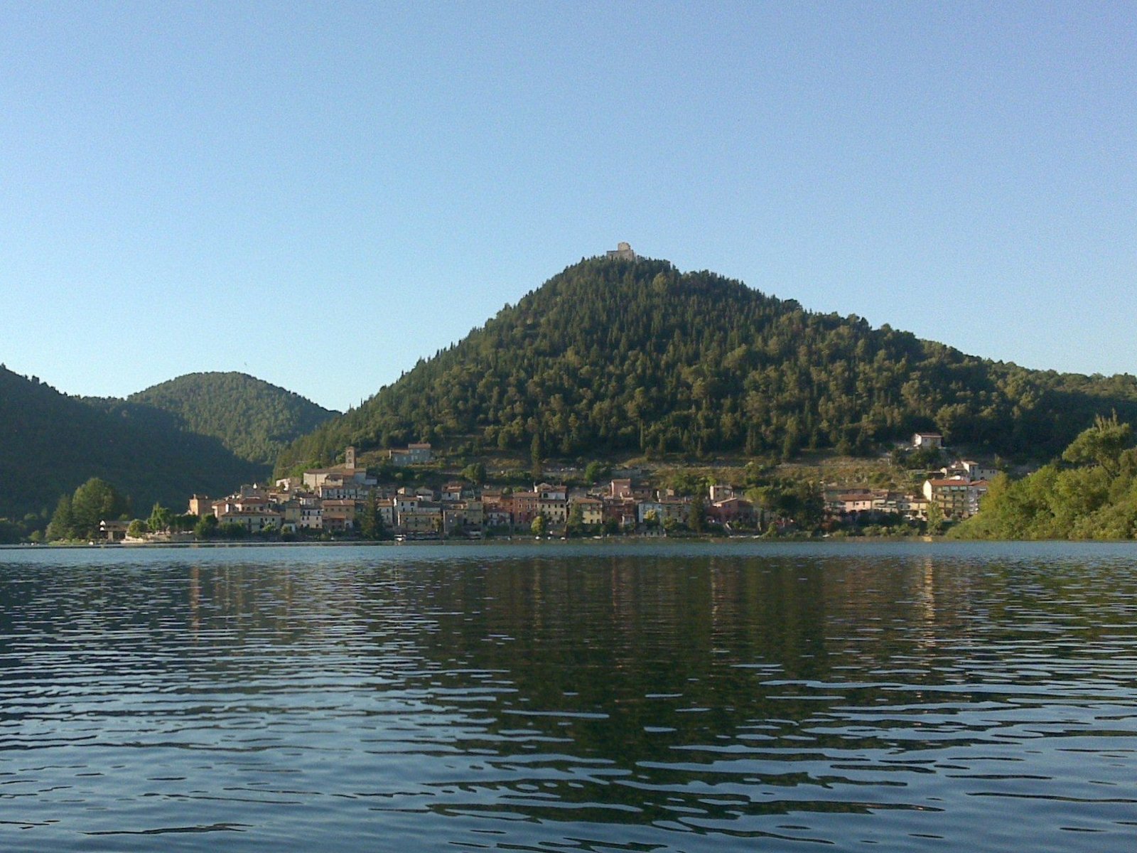 The village of Piediluco strung along the lakeshore beneath its steep wooded hill, seen from the water