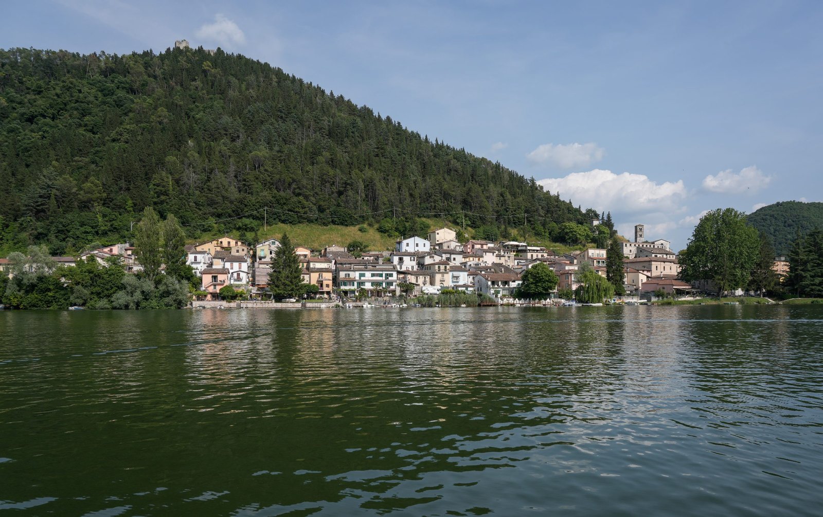 The village of Piediluco seen from a boat on the lake, its houses along the shore beneath a green hill