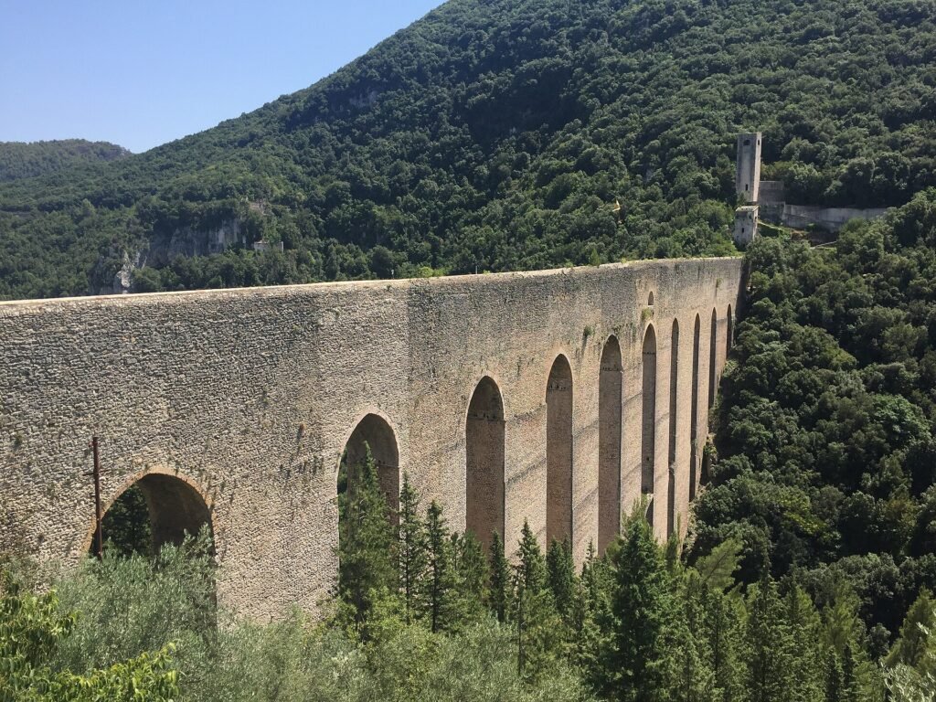 Le alte arcate in pietra del Ponte delle Torri sopra una gola boscosa, con una torre all’estremità
