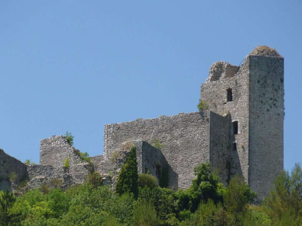 Mura in rovina della Rocca di Piediluco con un'alta torre spezzata in cima, alberi sotto e cielo azzurro