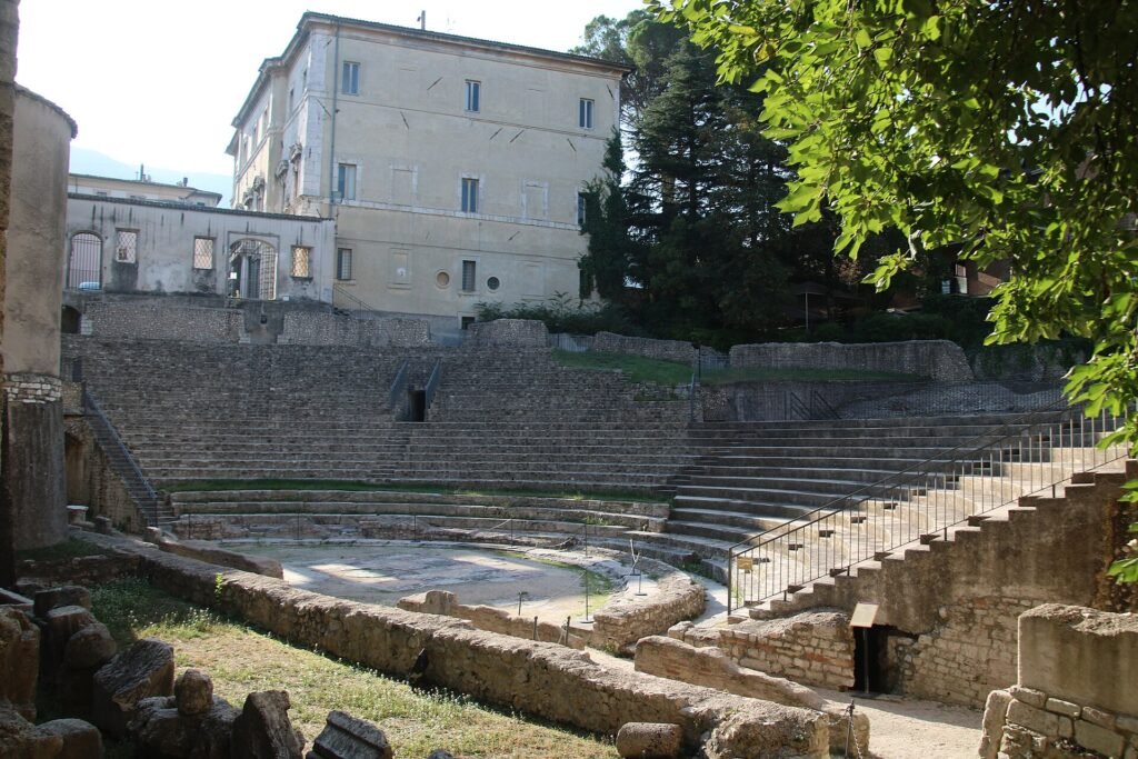 Le gradinate curve in pietra del teatro romano di Spoleto, con un alto palazzo chiaro alle spalle