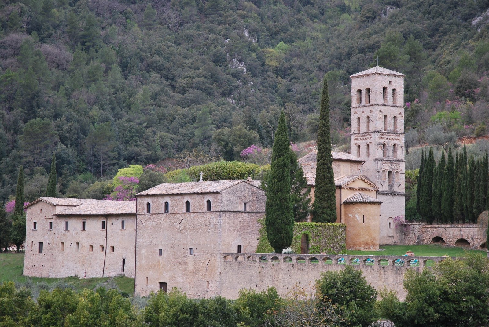 The abbey of San Pietro in Valle, its stone church and tall bell tower set against a wooded hillside