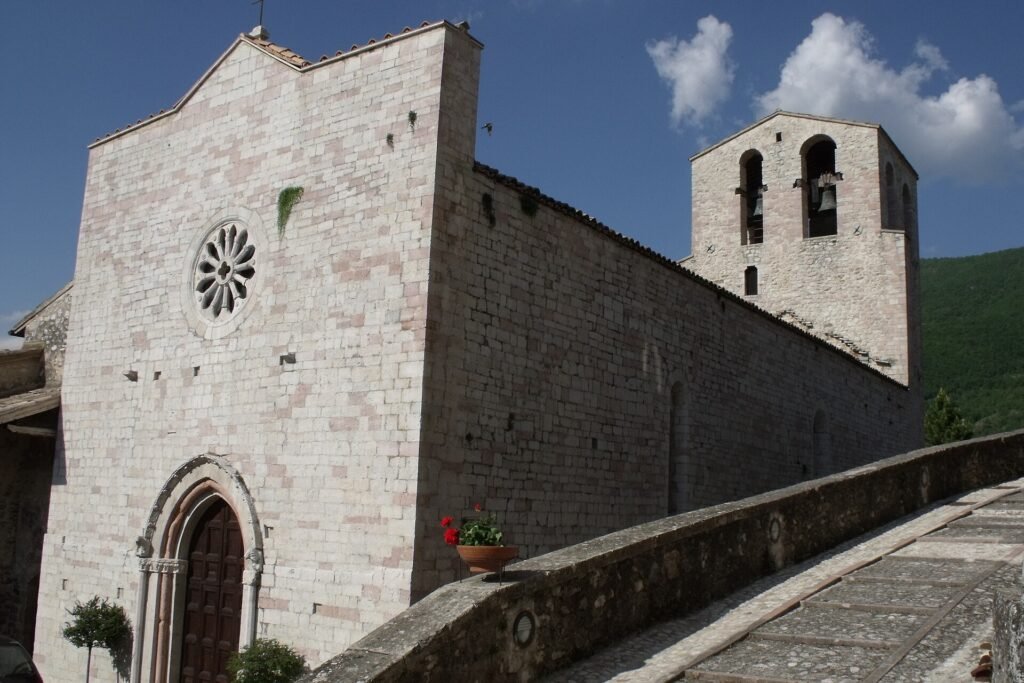 Facciata gotica in pietra con rosone e portale ogivale, accanto a un campanile quadrato