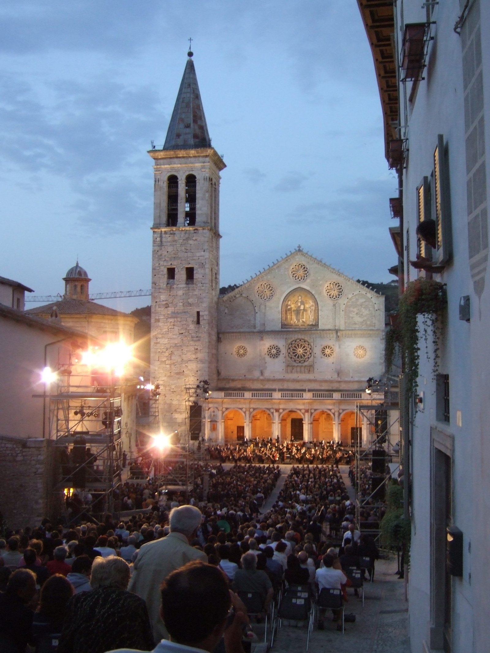 The lit facade of Spoleto cathedral at night above a packed audience seated in Piazza del Duomo during the festival