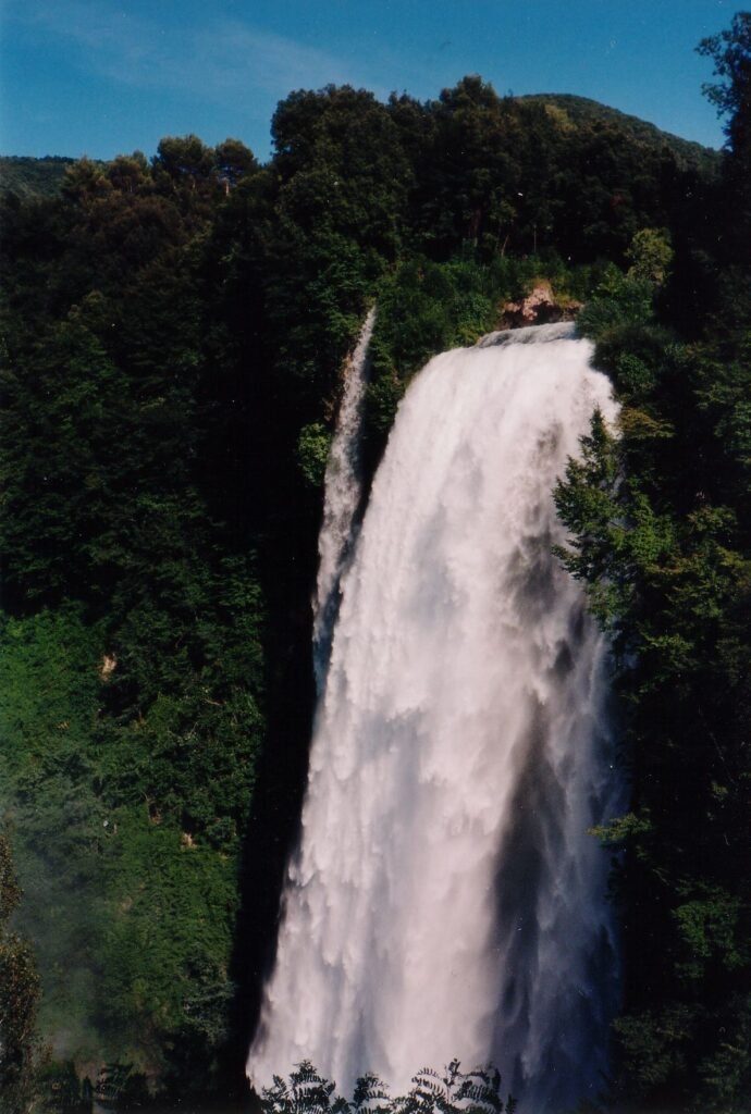 Vista dall'alto sul primo salto della Cascata delle Marmore, una colonna d'acqua bianca tra alberi verde scuro