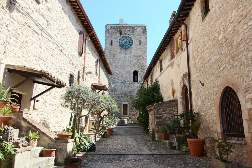 Vicolo in pietra con vasi di piante che porta a una torre quadrata in pietra con orologio