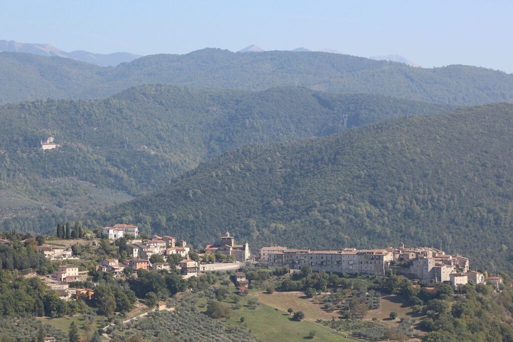 Il borgo di Torre Orsina disteso su un pendio verde di uliveti, con crinali boscosi alle spalle